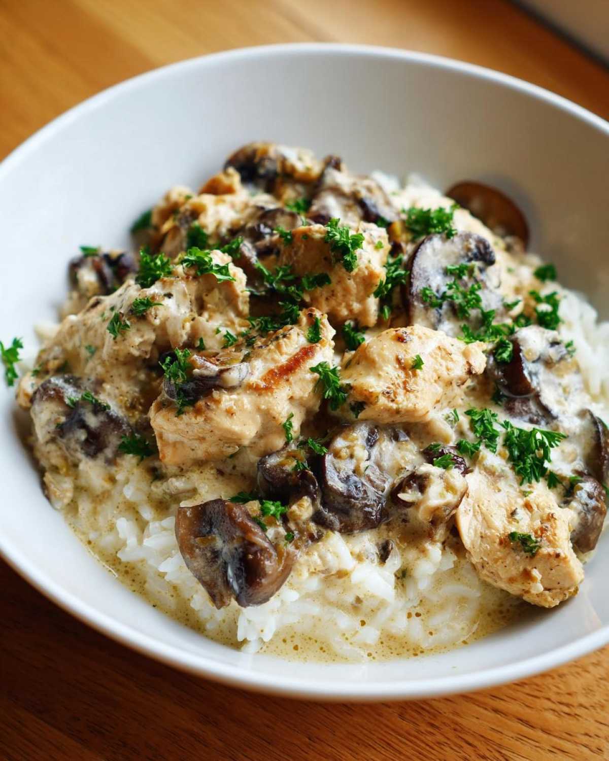 A white bowl filled with Creamy Mushroom Chicken and Rice Skillet, topped with fresh parsley.