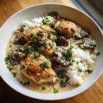 A close-up of a white bowl filled with Creamy Mushroom Chicken and Rice Skillet, topped with fresh parsley.