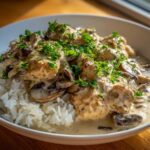 A white bowl filled with fluffy white rice topped with pieces of chicken and mushrooms in a rich, creamy sauce, garnished with fresh parsley, representing the Creamy Mushroom Chicken and Rice Skillet.