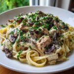 A close-up of rich Creamy Mushroom Chicken Pasta with Garlic Sauce, featuring fettuccine noodles, chunks of chicken, dark mushrooms, and fresh parsley.