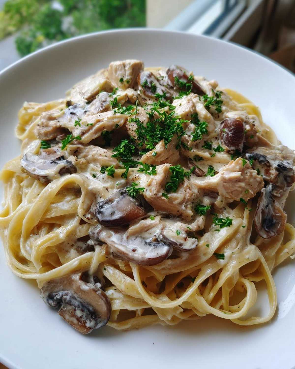A close-up of fettuccine pasta topped with chicken, sliced mushrooms, and a rich, creamy garlic sauce, garnished with parsley.