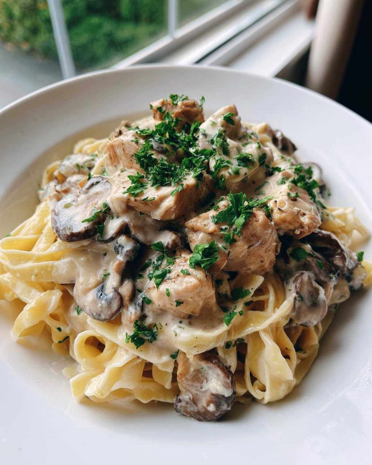 A close-up of fettuccine pasta topped with chicken, mushrooms, and rich garlic sauce, garnished with parsley for Creamy Mushroom Chicken Pasta.