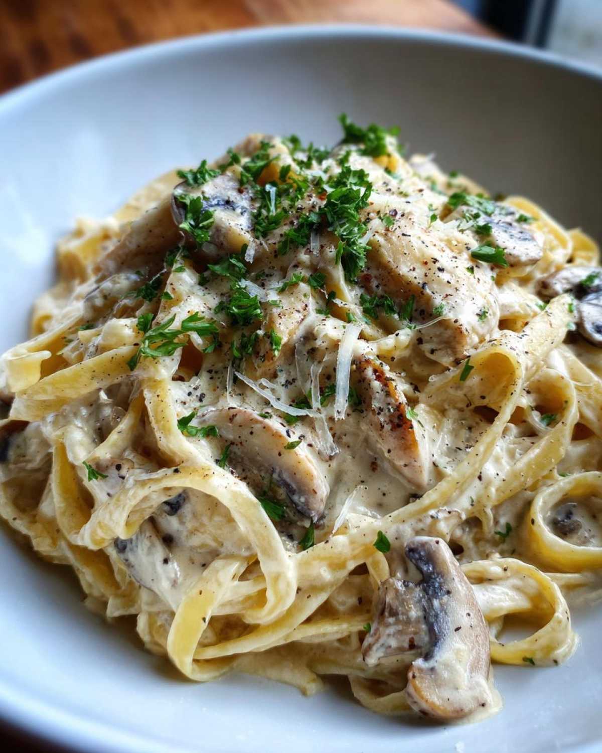 A close-up view of rich Creamy Mushroom Chicken Pasta with Parmesan, topped with fresh parsley and cracked black pepper.