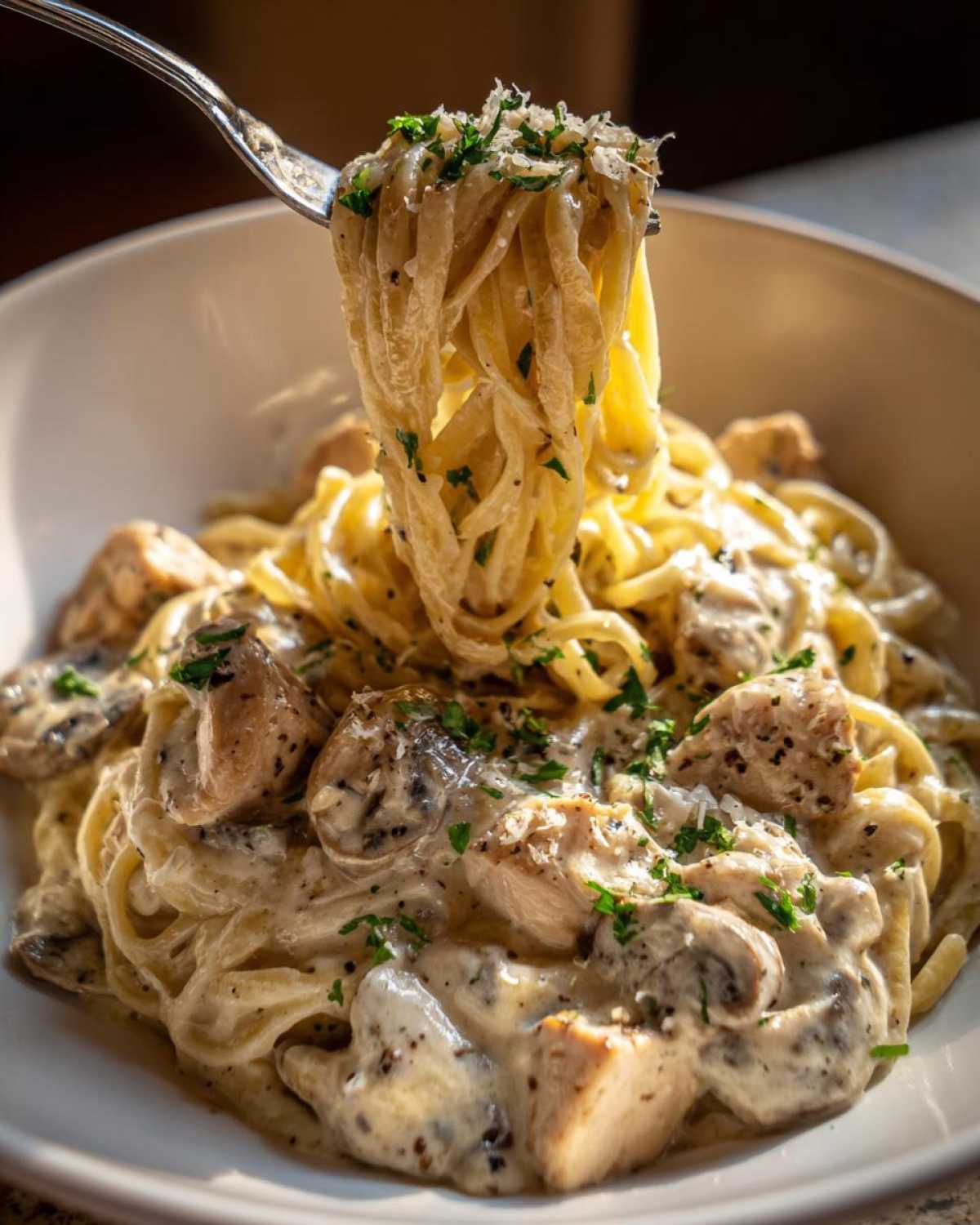 A fork lifts a twirl of pasta coated in sauce from a bowl of Creamy Mushroom Chicken Pasta with Parmesan.