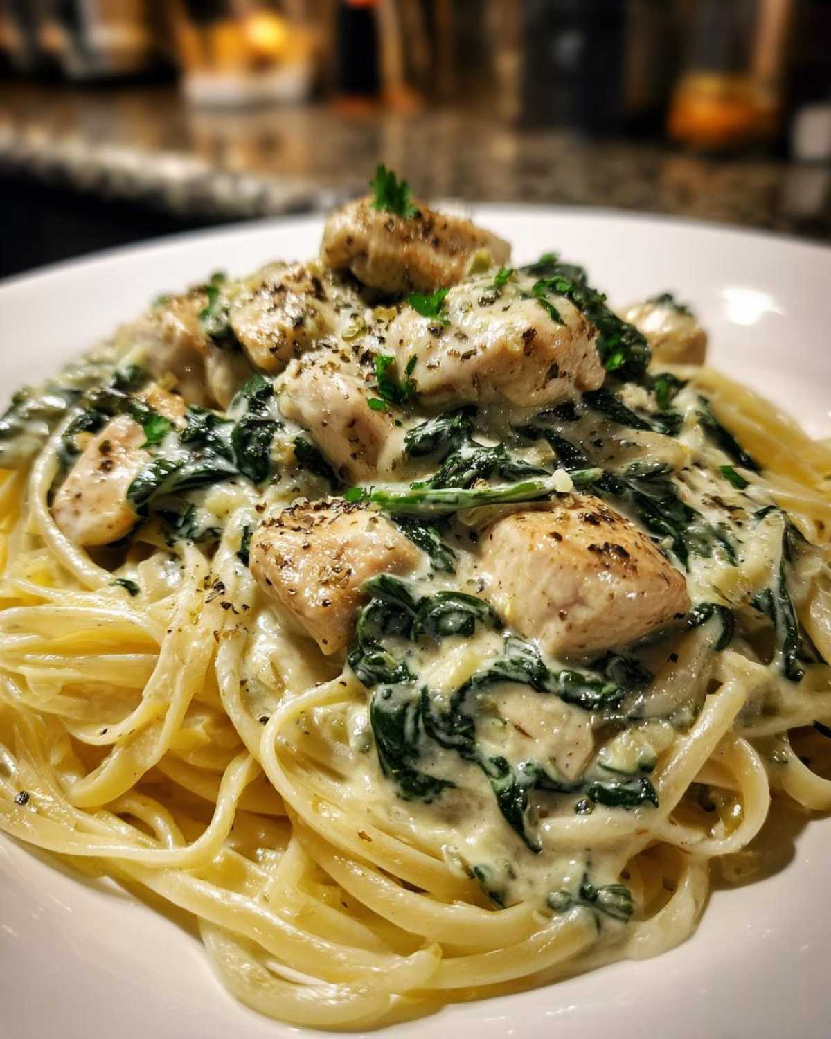 A close-up of fettuccine pasta topped with chicken pieces, wilted spinach, and rich Creamy Spinach Chicken Pasta with Alfredo Sauce.