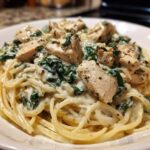 Close-up of a bowl of Creamy Spinach Chicken Pasta with Alfredo Sauce, featuring spaghetti, diced chicken, and wilted spinach.