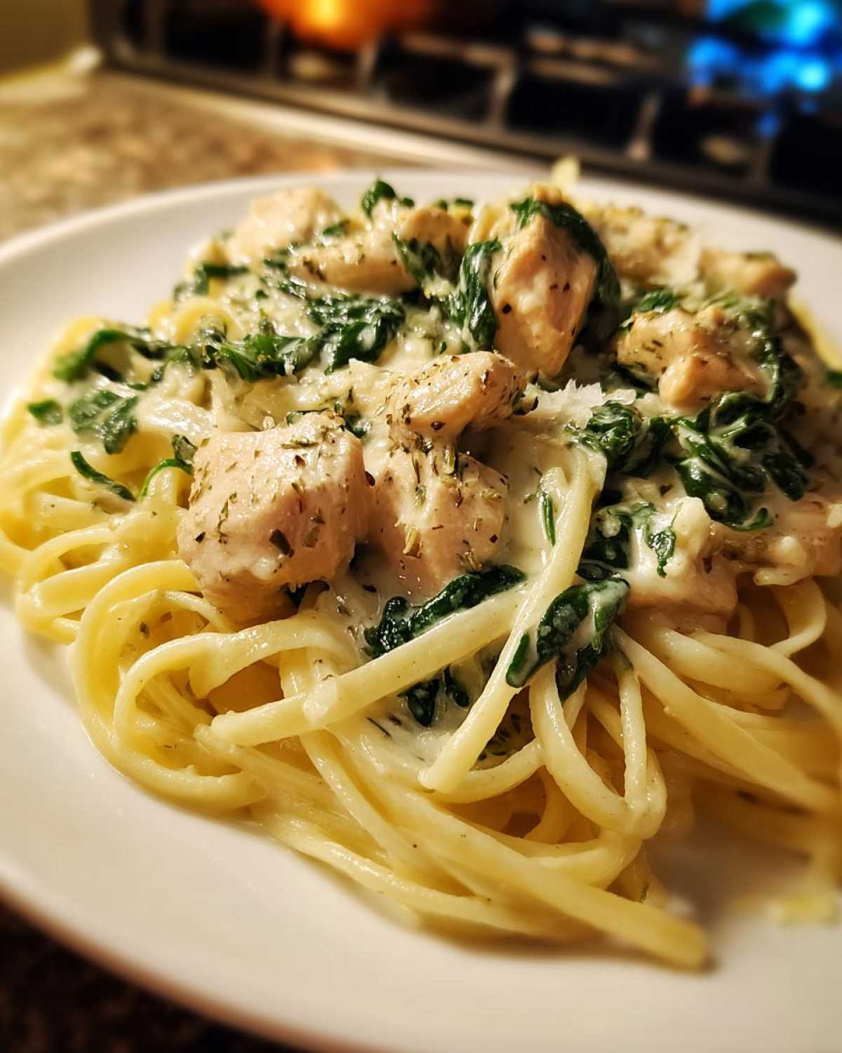 A close-up of a serving of Creamy Spinach Chicken Pasta with Alfredo Sauce, featuring linguine, chunks of seasoned chicken, and wilted spinach.