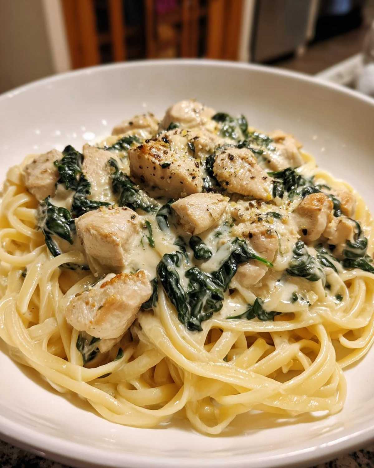 Close-up of Creamy Spinach Chicken Pasta with fettuccine noodles coated in Alfredo sauce, topped with seasoned chicken pieces.
