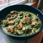 Golden seared chicken pieces swimming in a rich, creamy spinach and parmesan sauce in a black skillet.