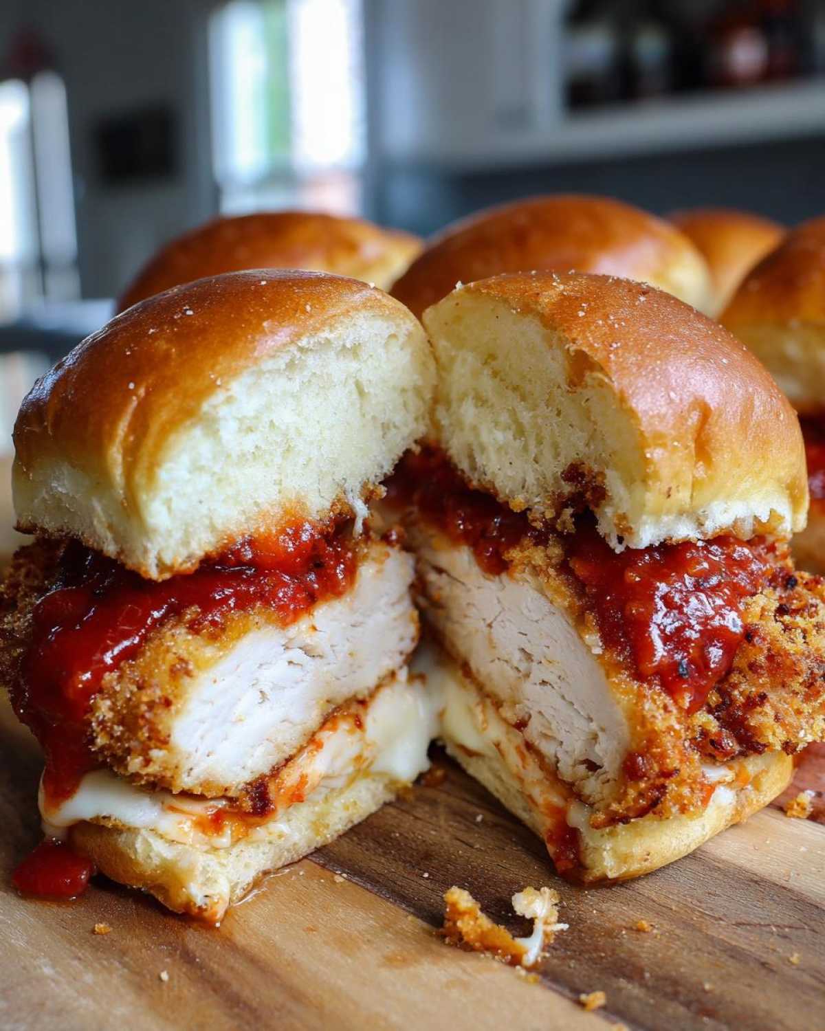 A close-up of Crispy Chicken Parmesan Sliders with Cheese cut in half, showing melted cheese and marinara sauce.