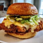 A close-up of a Crispy Chicken Sandwich with Garlic Parmesan Sauce, lettuce, and pickles on a brioche bun.