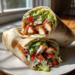 Two halves of a Crispy Chicken Wrap with Creamy Ranch Sauce, showing crispy chicken pieces, lettuce, and tomatoes.