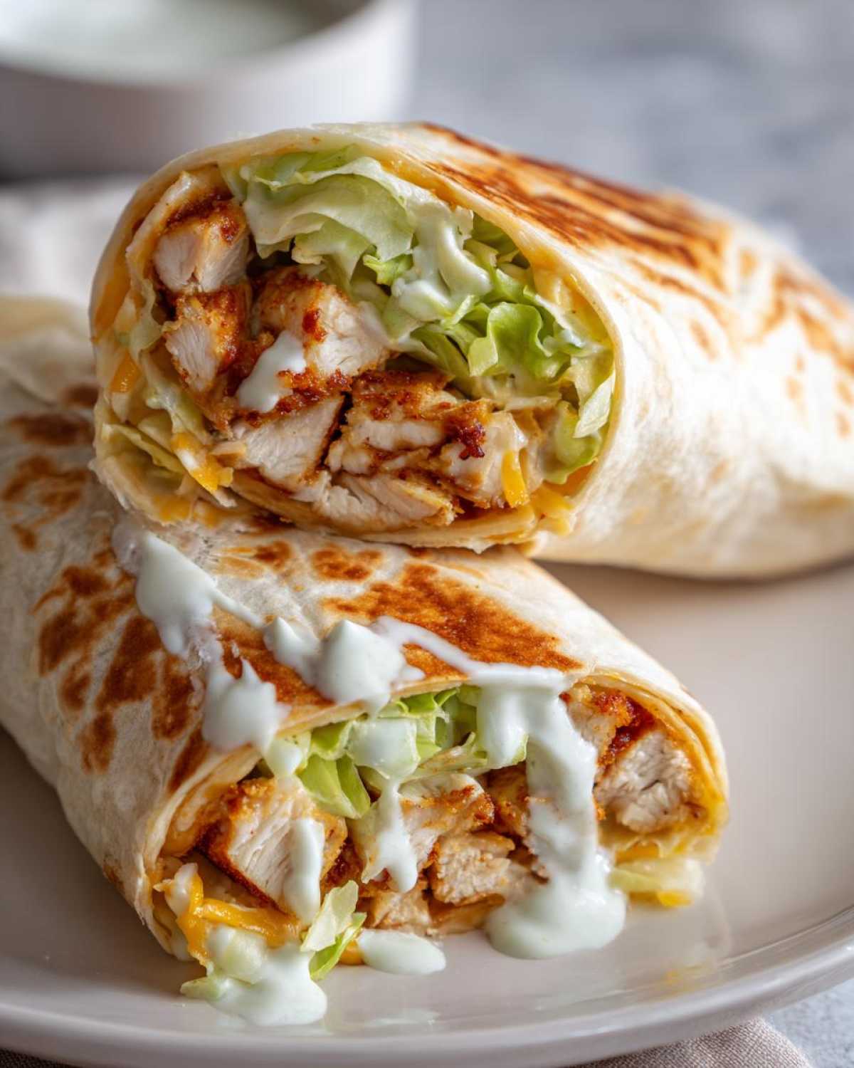 Two halves of a Crispy Chicken Wrap with Ranch Sauce, showing crispy chicken, lettuce, and ranch drizzle.