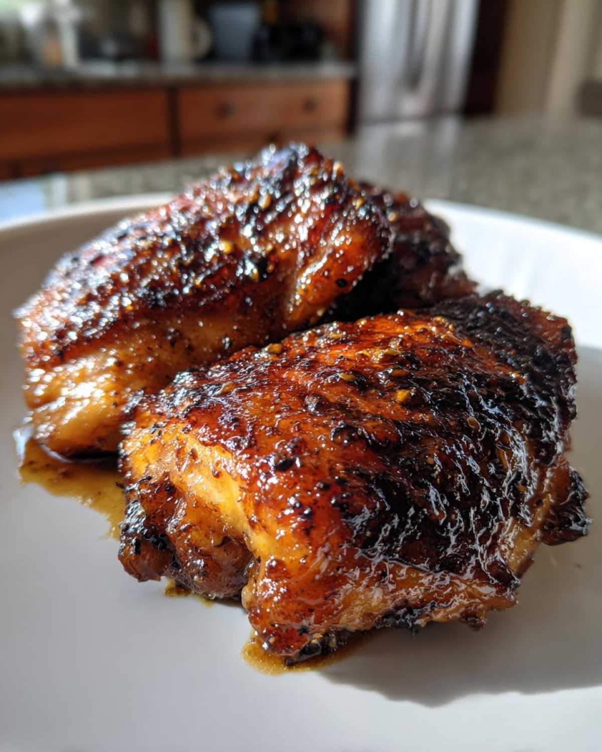 Close-up of three glistening Honey Soy Chicken Thighs with crispy, caramelized edges on a white plate.