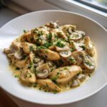 Close-up of tender chicken pieces and sliced mushrooms coated in a creamy garlic butter sauce, garnished with fresh parsley.