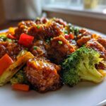 Close-up of glossy Garlic Butter Chicken Bites mixed with vibrant broccoli, red peppers, and carrots on a white plate.