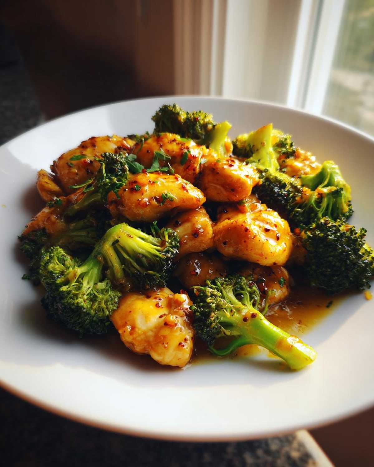 Close-up of Garlic Butter Chicken and Broccoli Stir Fry coated in a glossy sauce, served in a white bowl.