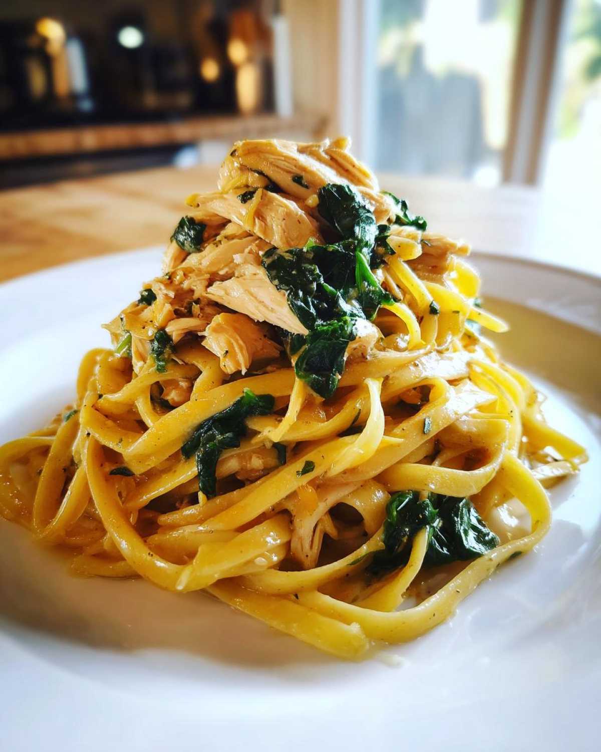 A tall serving of Garlic Butter Pasta with Chicken and Spinach tossed in a creamy sauce on a white plate.