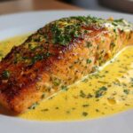 Close-up of perfectly cooked Garlic Butter Salmon topped with herbs, sitting in a rich, creamy lemon sauce.