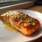 A perfectly cooked fillet of Garlic Butter Salmon with Lemon Garlic Sauce glistening on a white plate.