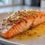Close-up of a perfectly cooked fillet of Garlic Butter Salmon with Lemon Garlic Sauce pooled around it.