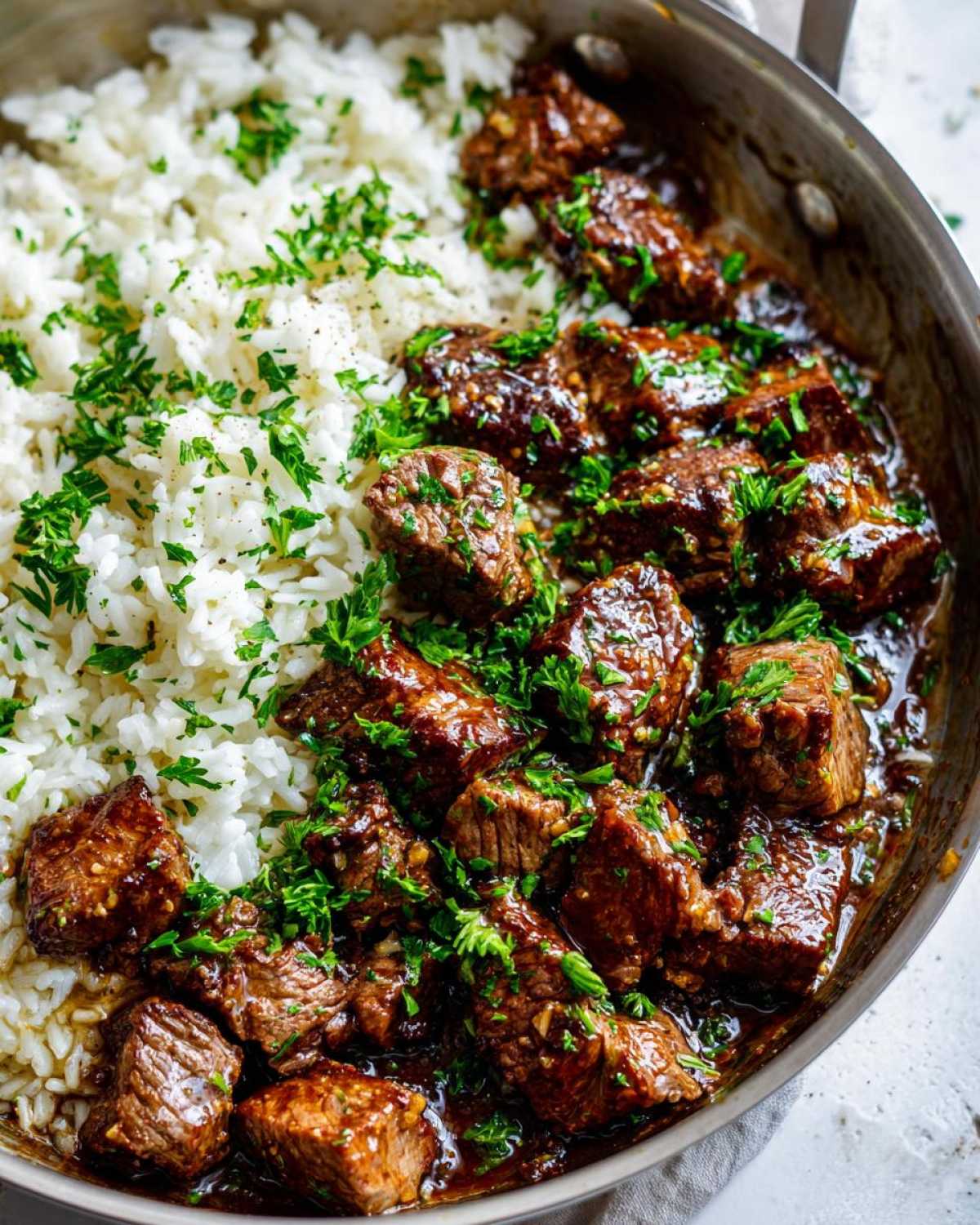 Close-up of Garlic Butter Steak and Rice Skillet Dinner, featuring saucy steak cubes next to white rice, garnished with parsley.