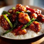 Close-up of sticky, glazed Honey Garlic Chicken Bites served over a bed of white rice, garnished with green onions and sesame seeds.