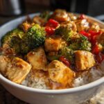 Close-up of a Honey Garlic Chicken Bowl with rice, broccoli, and red peppers coated in a glossy sauce.