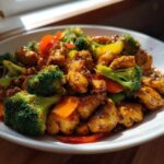 Close-up of a white bowl filled with glossy Honey Garlic Chicken and Veggie Stir Fry featuring broccoli, carrots, and peppers.