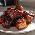A pile of glistening Honey Garlic Salmon Bites with caramelized edges and sesame seeds on a white plate.