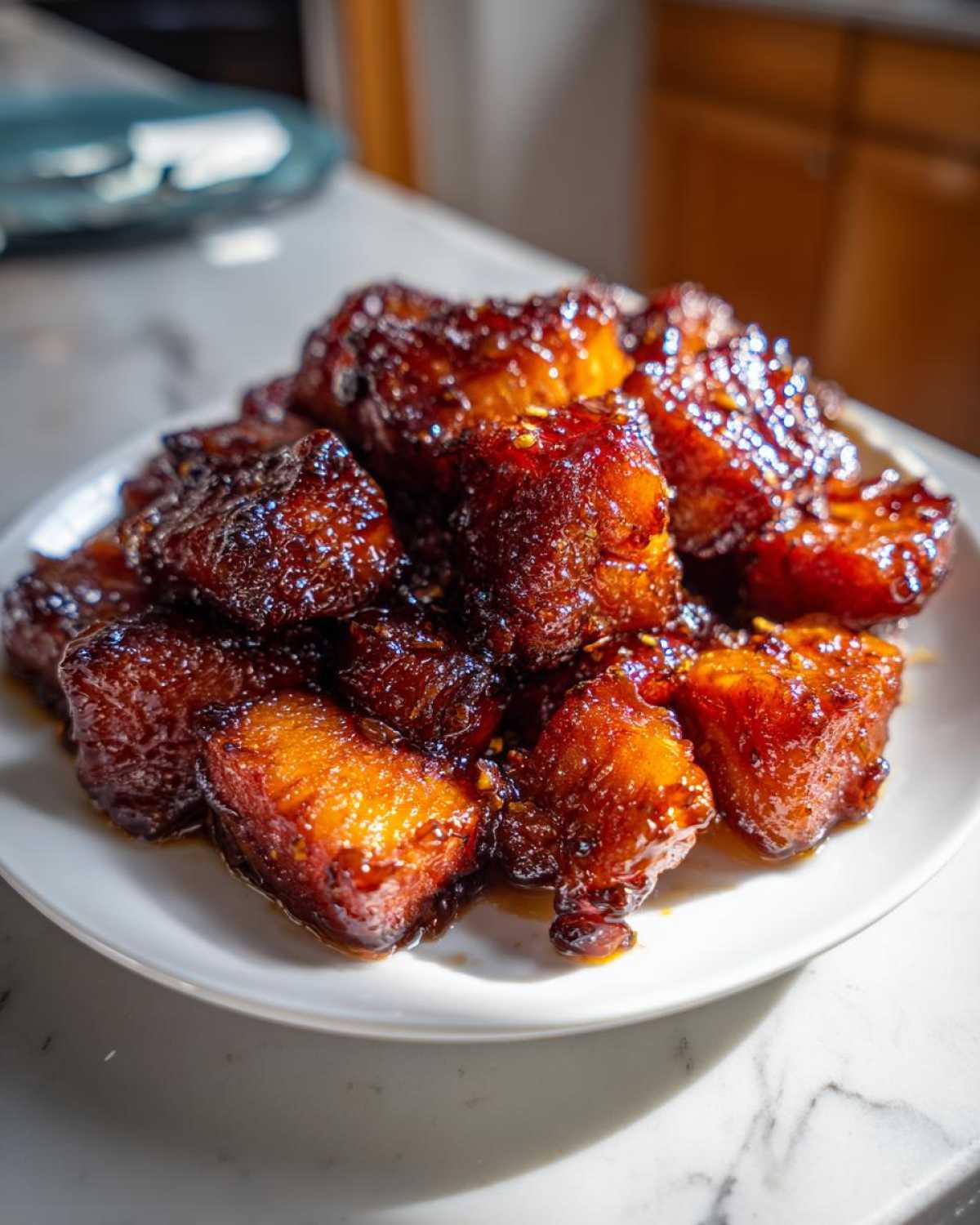 A close-up of glistening Honey Garlic Salmon Bites piled high on a white plate, showing caramelized edges.