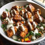 Close-up of a Honey Mustard Chicken Bowl featuring glazed chicken pieces over quinoa and greens, drizzled with creamy sauce.