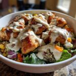 Close-up of a Honey Mustard Chicken Bowl featuring glazed chicken pieces topped with a generous drizzle of creamy sauce over quinoa and greens.