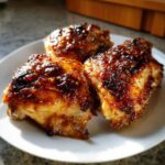 Three pieces of perfectly cooked Honey Mustard Chicken Thighs Oven Roasted with a dark, glossy glaze served on a white plate.