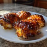 Four glistening Honey Mustard Chicken Thighs Oven Roasted on a white plate with a sticky, caramelized glaze.