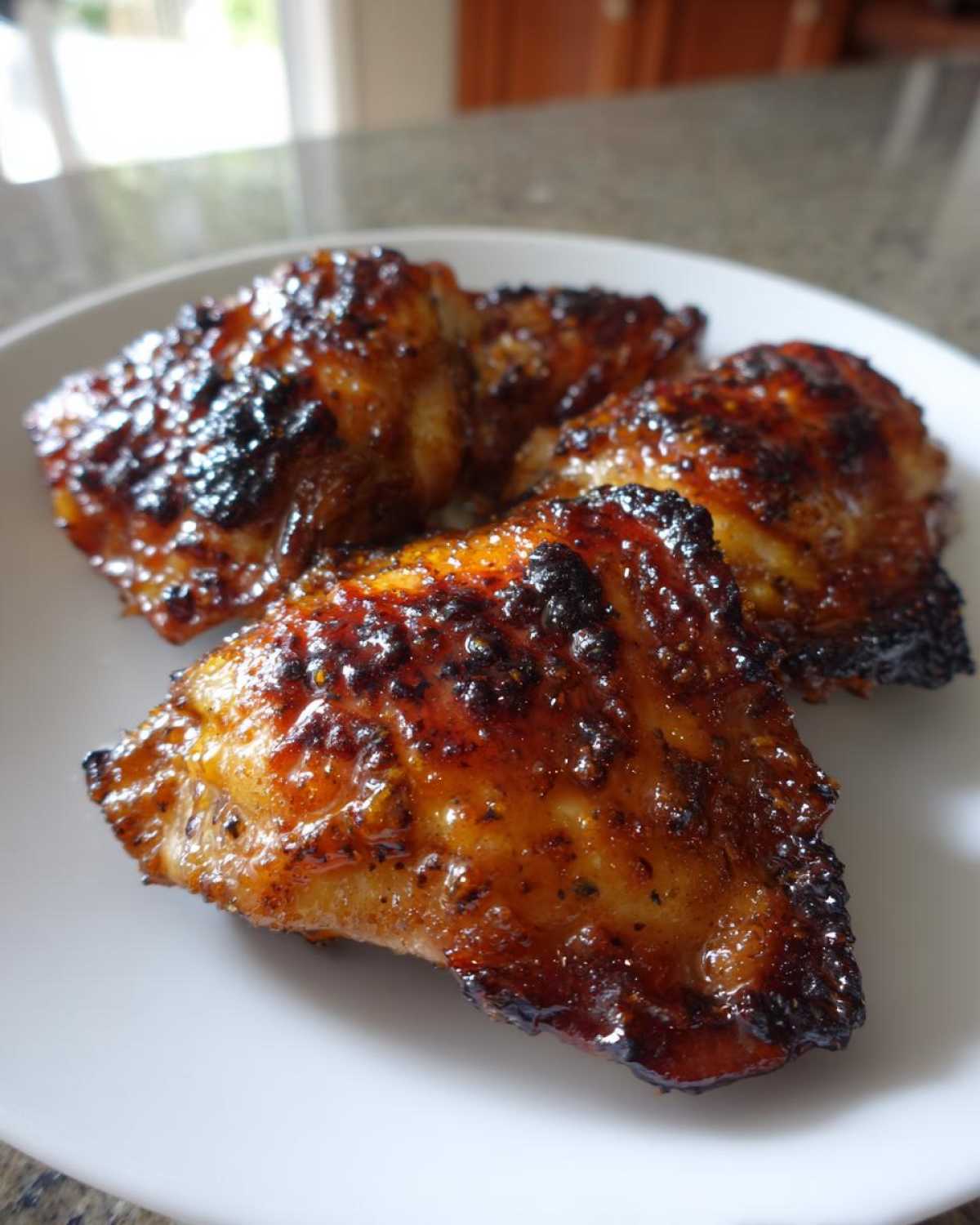 Close-up of four glistening, caramelized Honey Mustard Chicken Thighs Oven Roasted pieces on a white plate.
