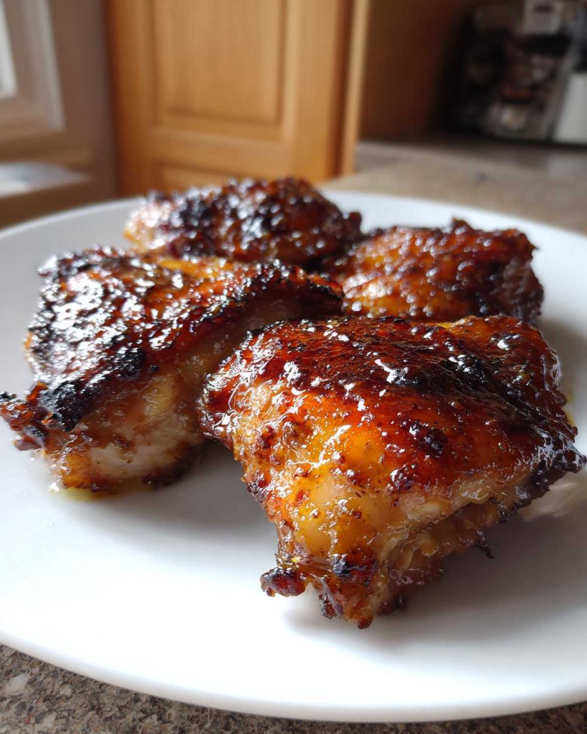 Close-up of four glistening, oven-roasted Honey Mustard Chicken Thighs with a caramelized glaze on a white plate.