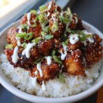 Close-up of a Honey Soy Chicken Bowl with crispy chicken pieces coated in glaze, served over white rice and drizzled with garlic sauce.