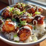 Close-up of a Honey Soy Chicken Bowl with Garlic Sauce, featuring glazed chicken pieces over white rice, drizzled with white sauce and topped with sesame seeds and scallions.