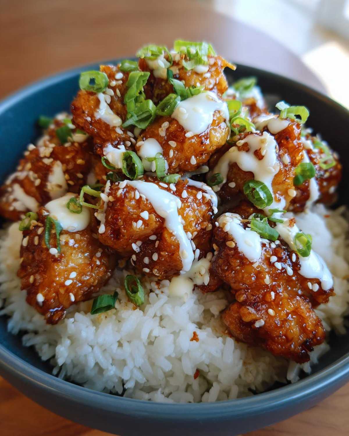 Close-up of a Honey Soy Chicken Bowl with garlic sauce drizzled over glazed chicken pieces served on white rice.