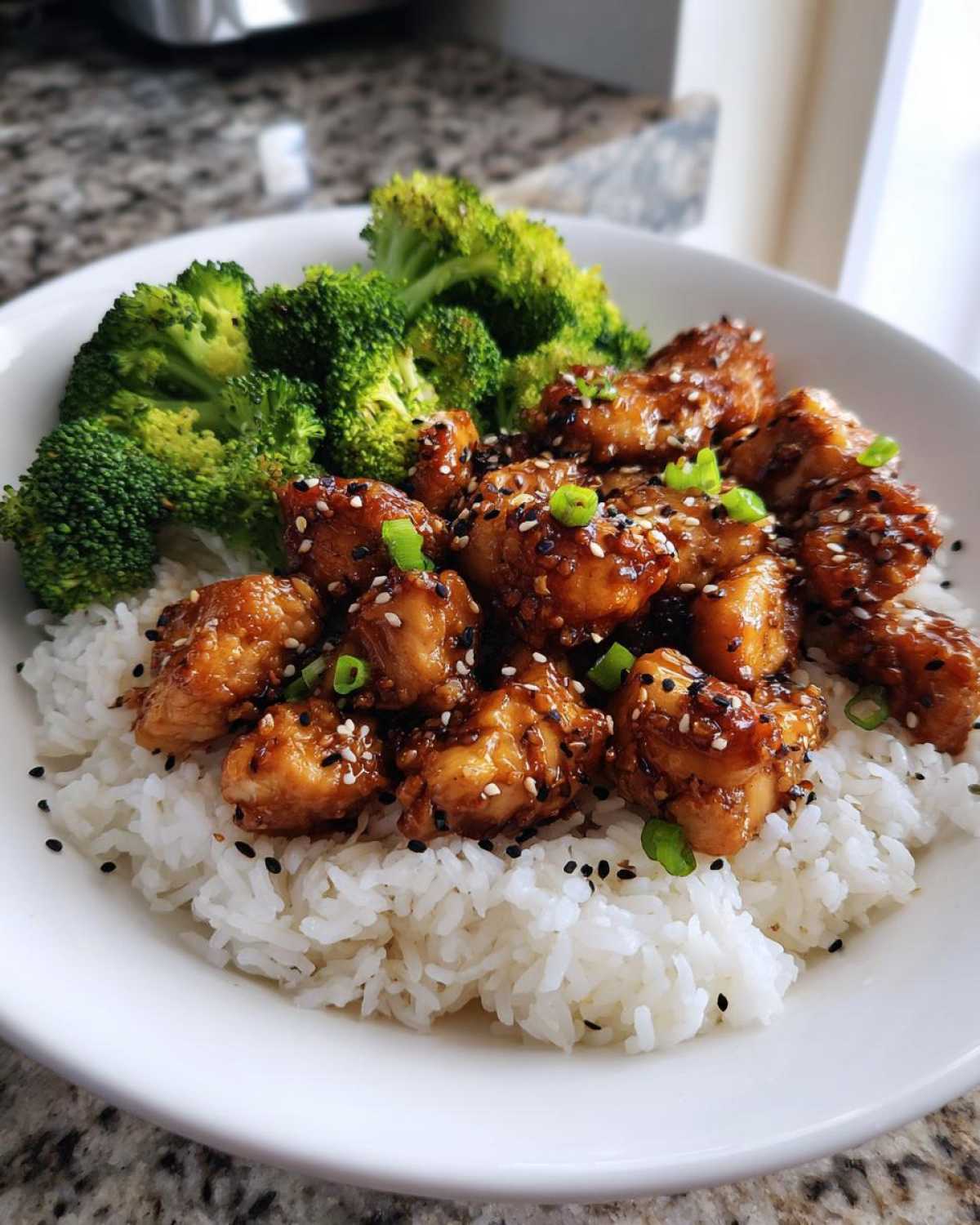 A close-up of a white bowl filled with white rice topped with glazed Honey Soy Garlic Chicken and steamed broccoli.