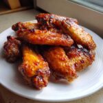 A pile of glossy, glazed Honey Sriracha Chicken Wings Crispy Oven Baked stacked on a white plate.