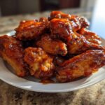 A plate piled high with sticky and crispy Honey Sriracha Chicken Wings coated in a glossy, reddish-brown glaze.