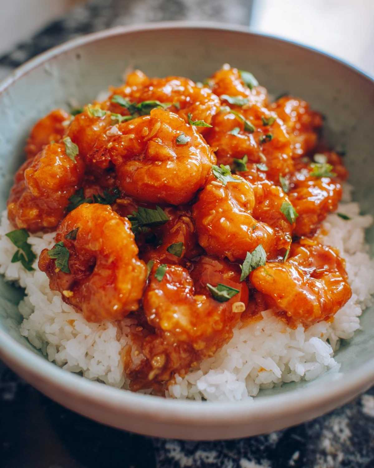 Close-up of Honey Sriracha Shrimp Bowl with Rice, featuring glazed shrimp piled on white rice and garnished with herbs.