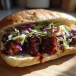 A close-up of a Sticky BBQ Chicken Sandwich overflowing with dark, glossy sauce and topped with vibrant, crunchy coleslaw.
