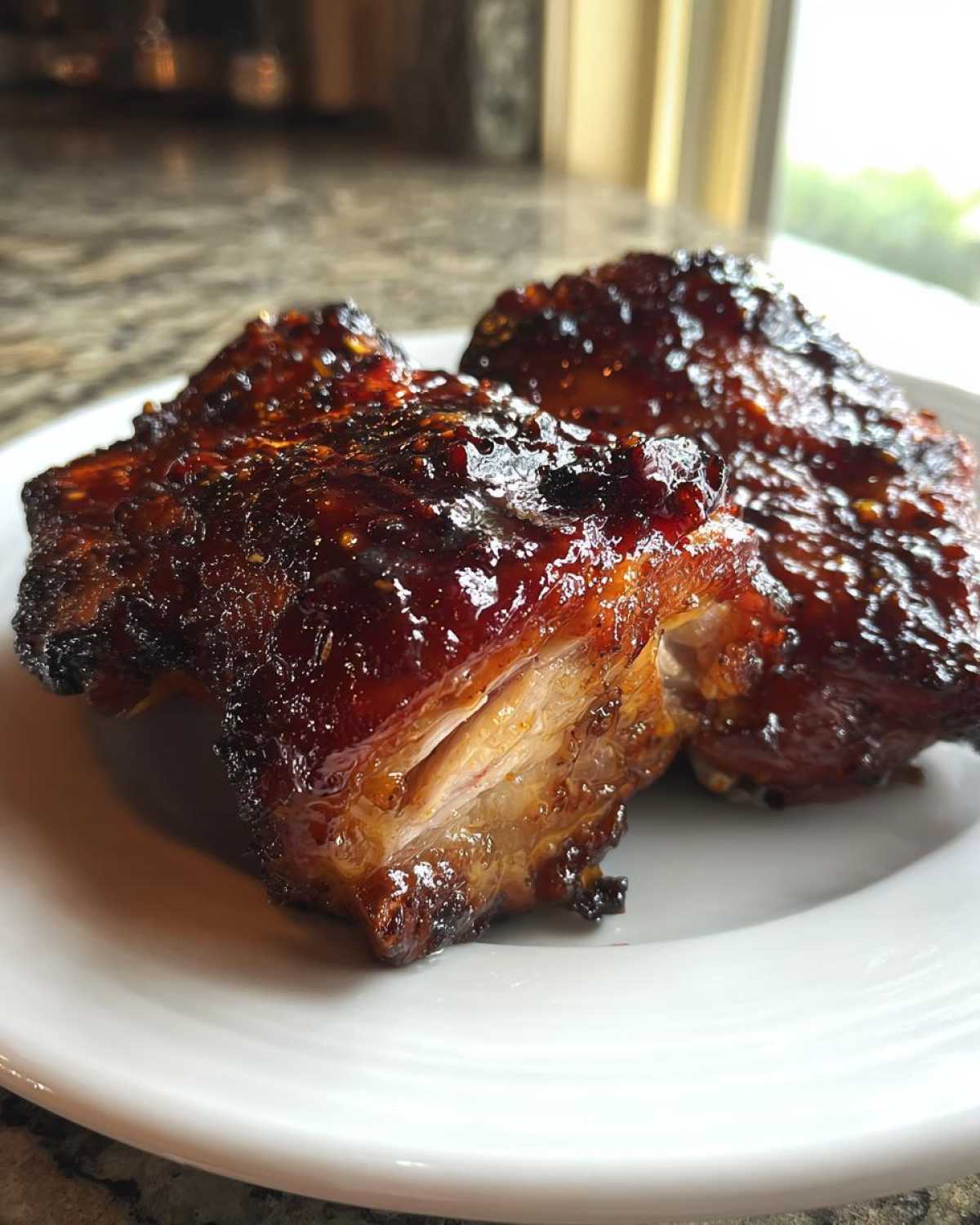 Two pieces of juicy Sticky BBQ Chicken Thighs with Honey Glaze, showing a dark, caramelized, and glossy exterior on a white plate.