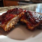 Two pieces of tender Sticky BBQ Chicken Thighs with Honey Glaze cut open on a white plate.