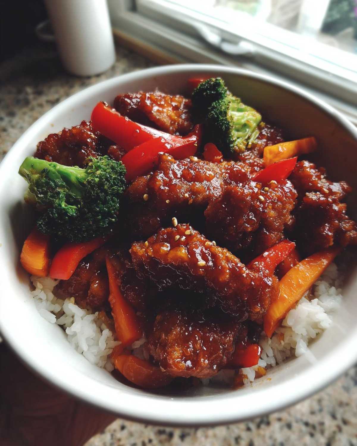 Close-up of a Sticky Orange Chicken Bowl featuring glazed chicken pieces, bright red peppers, broccoli florets, and white rice.