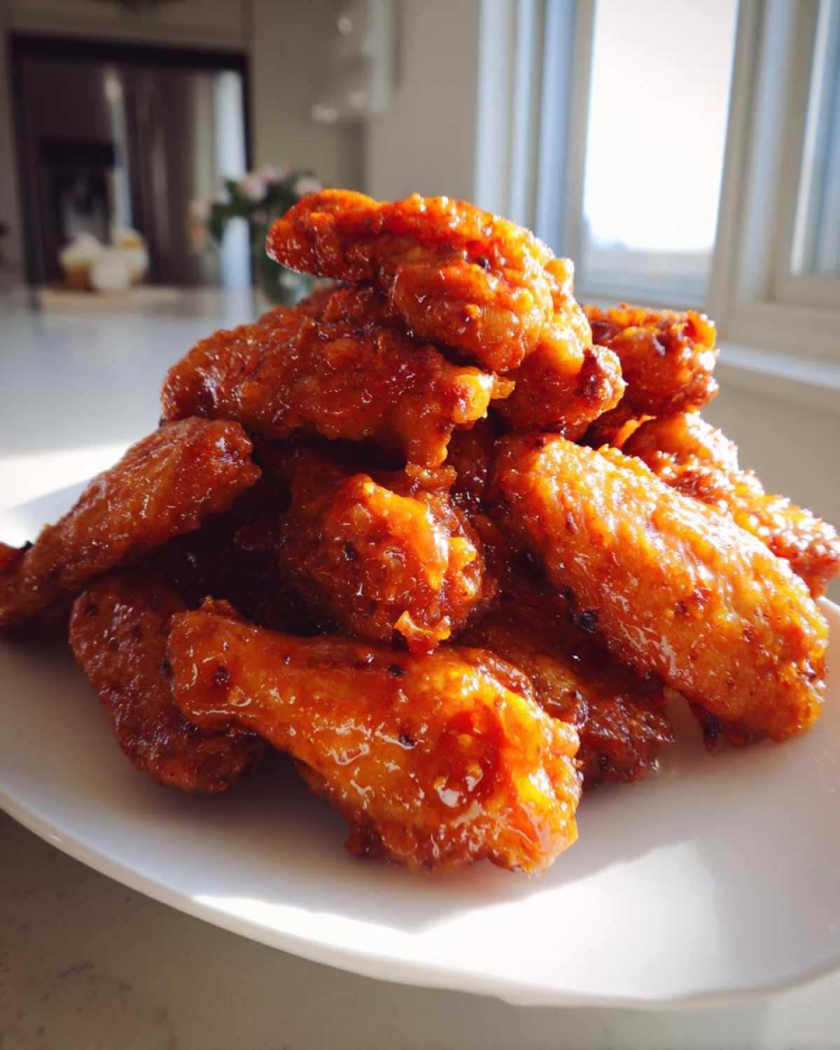 A close-up mound of glistening Sticky Orange Chicken Wings with Honey Glaze piled high on a white plate.