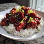 Close-up of Sticky Sweet Chili Chicken Skillet pieces coated in dark glaze served over white rice, garnished with green onions and sesame seeds.